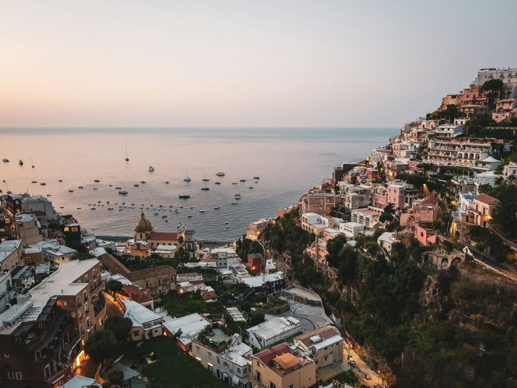 Elevated view of Positano, coastal buildings, and boats on the Amalfi Coast at sunset.